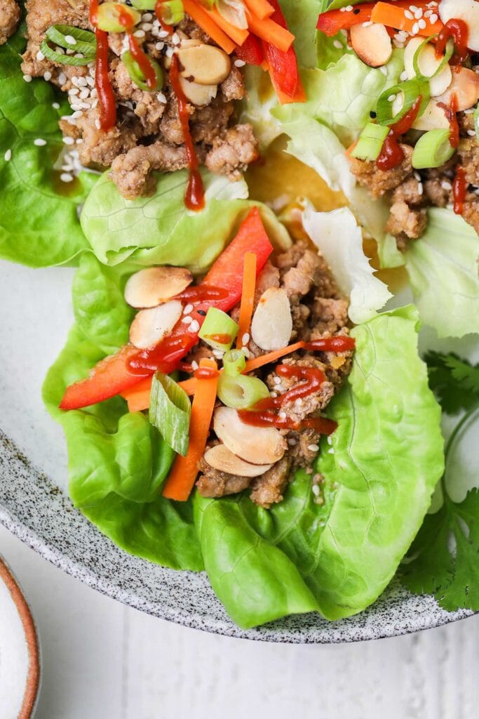 A close up of a pork lettuce wrap with a drizzle of sriracha hot sauce on top.