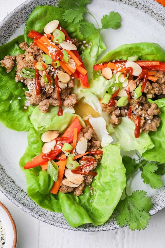 A plate of pork lettuce wraps shown drizzled with chili sauce.