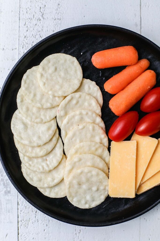 A photo of rice crackers on a plate with vegetables and cheese.