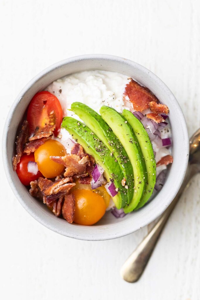 A bowl of cottage cheese topped with bacon and avocado.