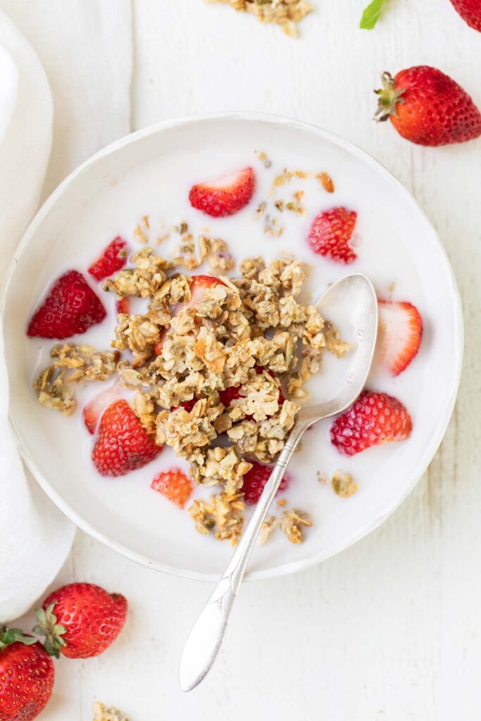 A bowl of strawberries and keto granola shown with almond milk.